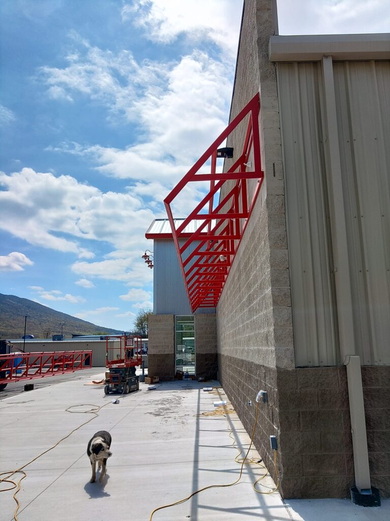 Custom steel canopy frame installation on a commercial building exterior for covered walkway and structural expansion.