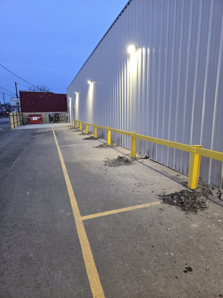 Commercial safety guardrail installation along a warehouse exterior to protect building walls and loading area traffic.
