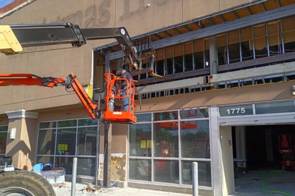 Structural steel framing installation underway for a commercial storefront expansion using aerial lift equipment and custom steel beams.